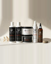Kuruve Chebe shampoo, conditioner, hair pudding, Sealant Butter, Hydration & Detangle Spray, and oil lined up on a light countertop